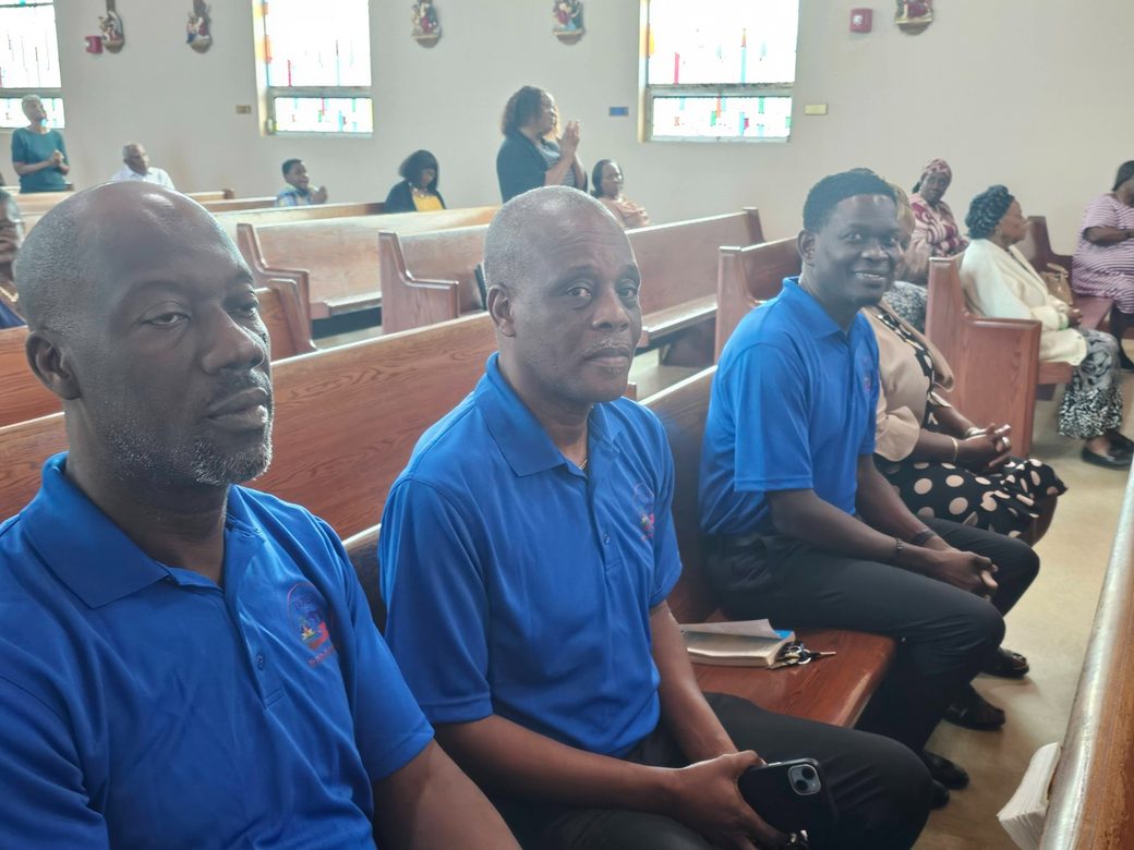 Three HTHH volunteers in blue branded shirts seated in a church congregation.